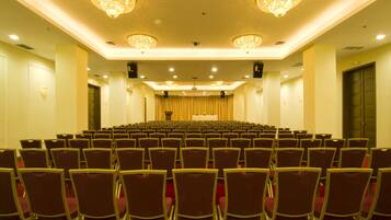 Een congreszaal met rijen stoelen, een podium en kroonluchters.