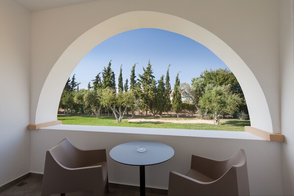 Una habitación con una mesa redonda y dos sillas, un ventanal con vistas en arco a árboles y césped.