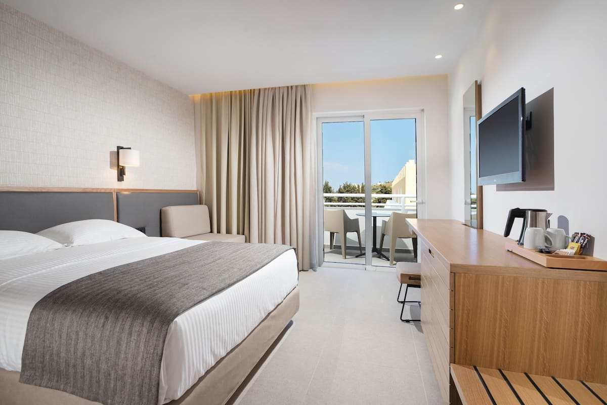 A modern hotel room with a large bed, a desk, a flat-screen TV, and a balcony with a view.