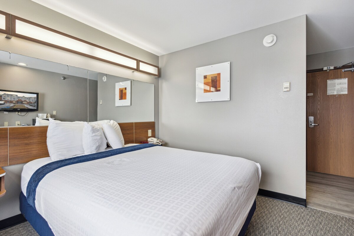 A hotel room with a large bed, a wooden headboard, a flat-screen TV, a mirror, and a door with a wooden panel.