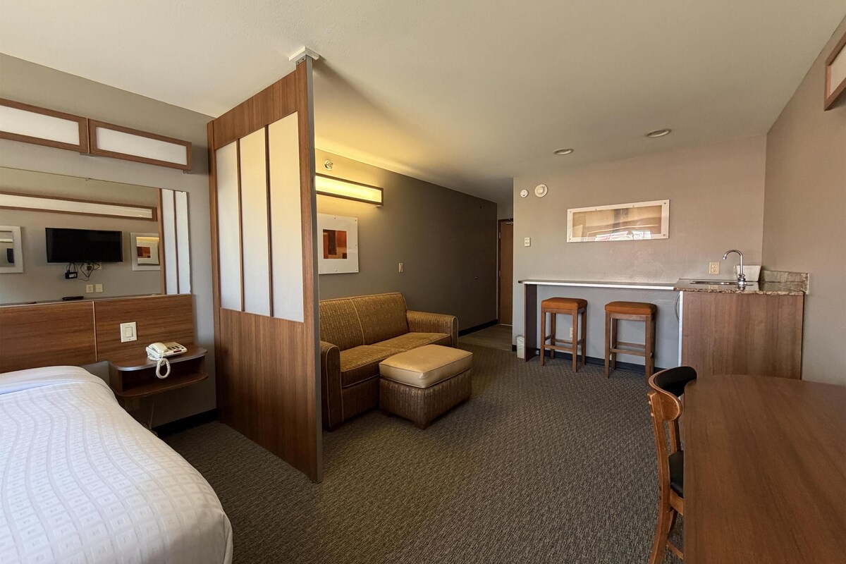 Habitación de hotel con cama, sofá, un pequeño comedor con taburetes, televisor y escritorio con teléfono.
