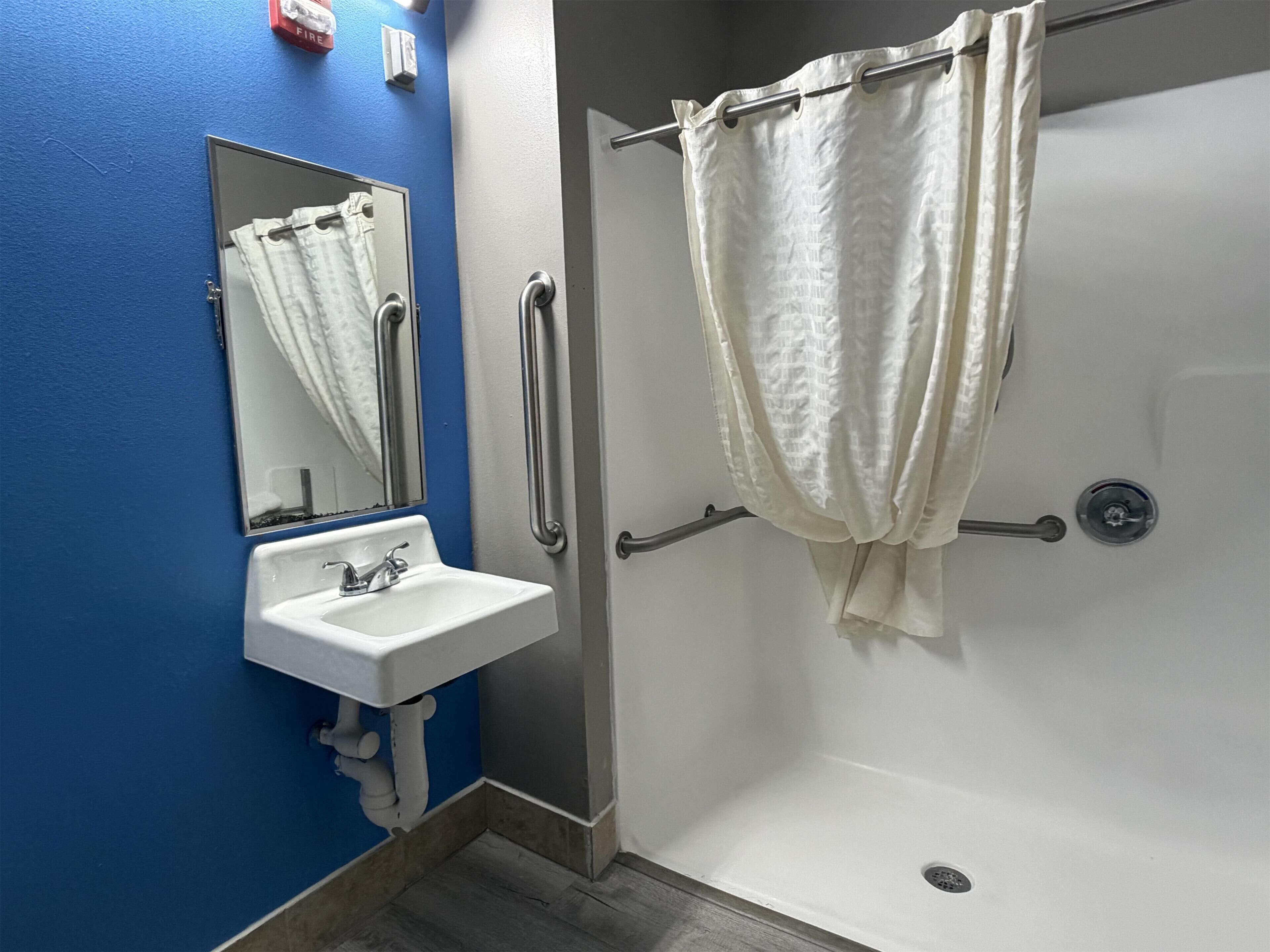 Une salle de bain avec un lavabo blanc, un miroir, une douche avec un rideau blanc et un mur bleu.