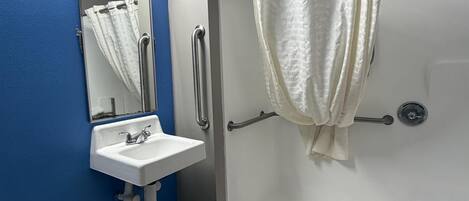 Une salle de bain avec un lavabo blanc, un miroir, une douche avec un rideau blanc et un mur bleu.