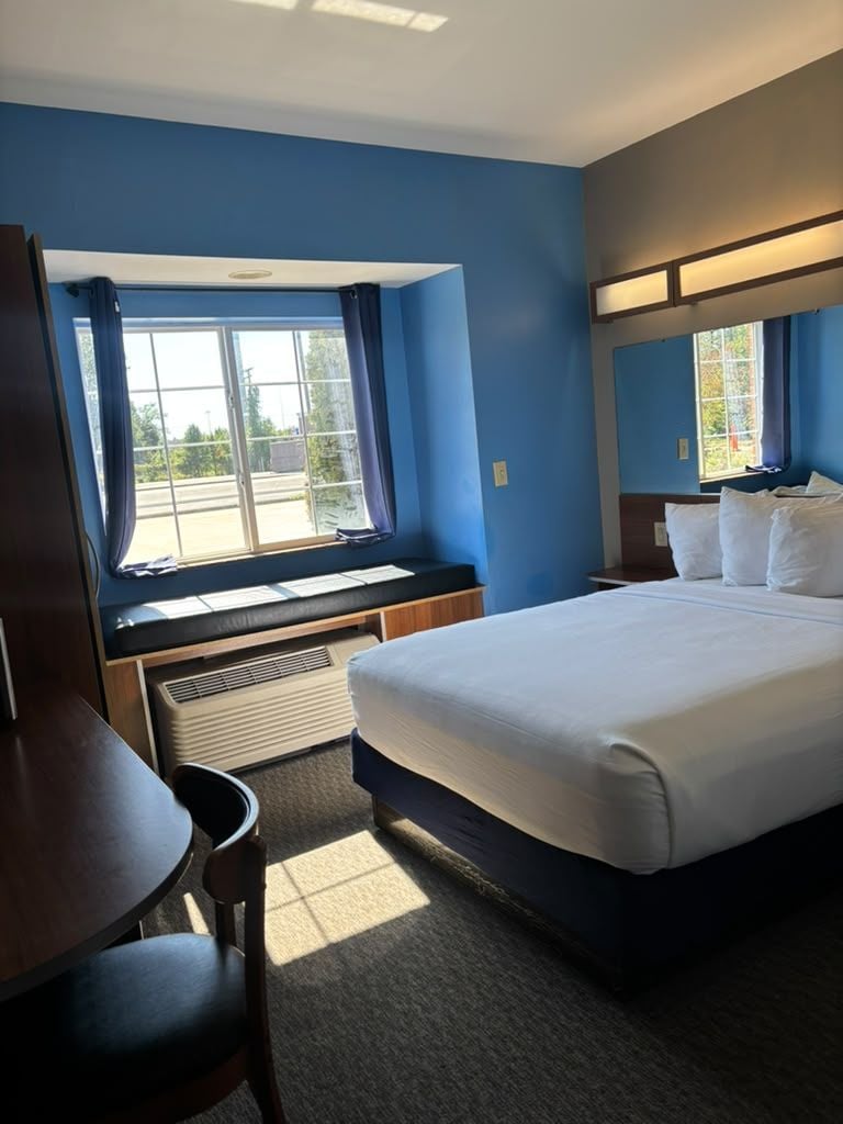A hotel room with a bed, a desk, and a window with curtains.