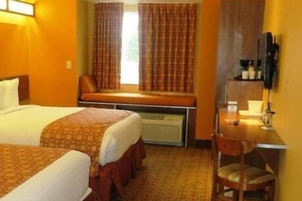 Une chambre d’hôtel avec deux lits, un bureau, une chaise, une fenêtre avec des rideaux et un téléviseur.