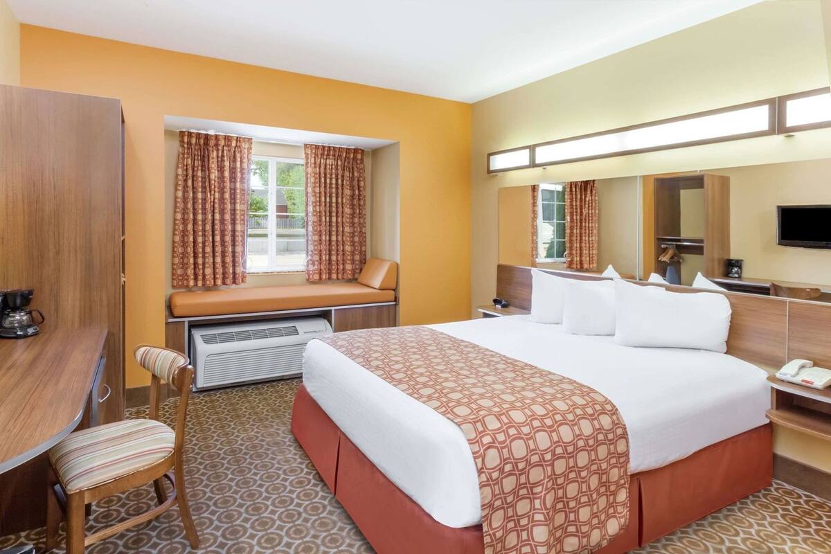 Une chambre d’hôtel comprenant un lit, un bureau, une chaise, une fenêtre avec des rideaux, un radiateur, un miroir et un téléviseur.