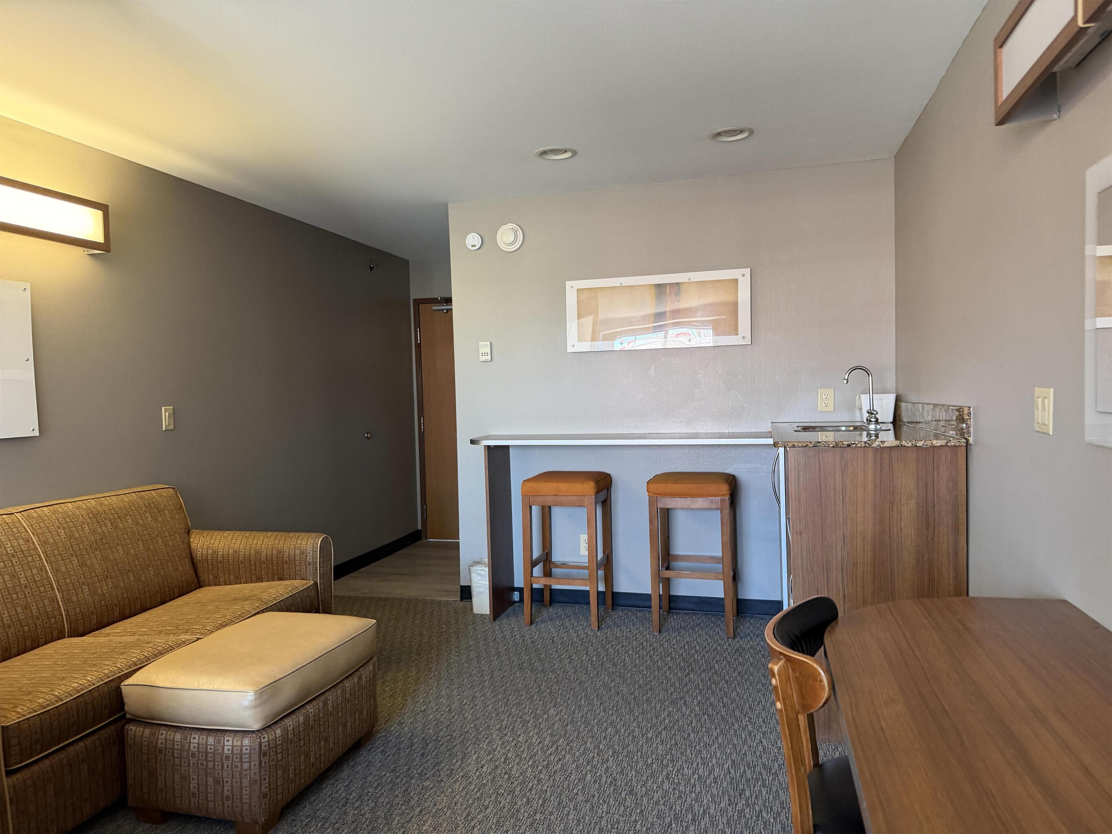 A compact living space with a kitchenette, a sofa, a dining table, and two bar stools.