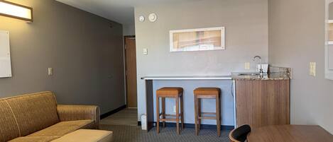 A compact living space with a kitchenette, a sofa, a dining table, and two bar stools.