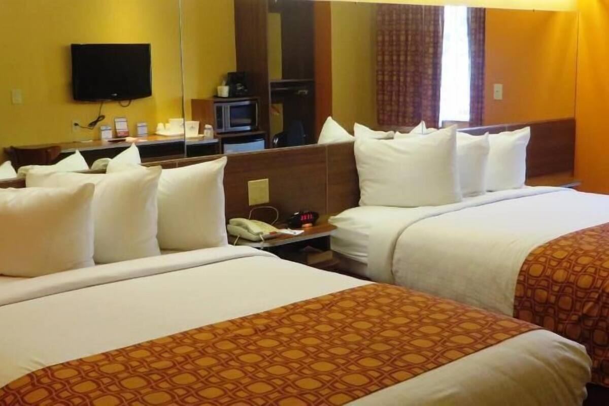 Une chambre d’hôtel avec deux lits, une télévision, un bureau avec un téléphone et un miroir.