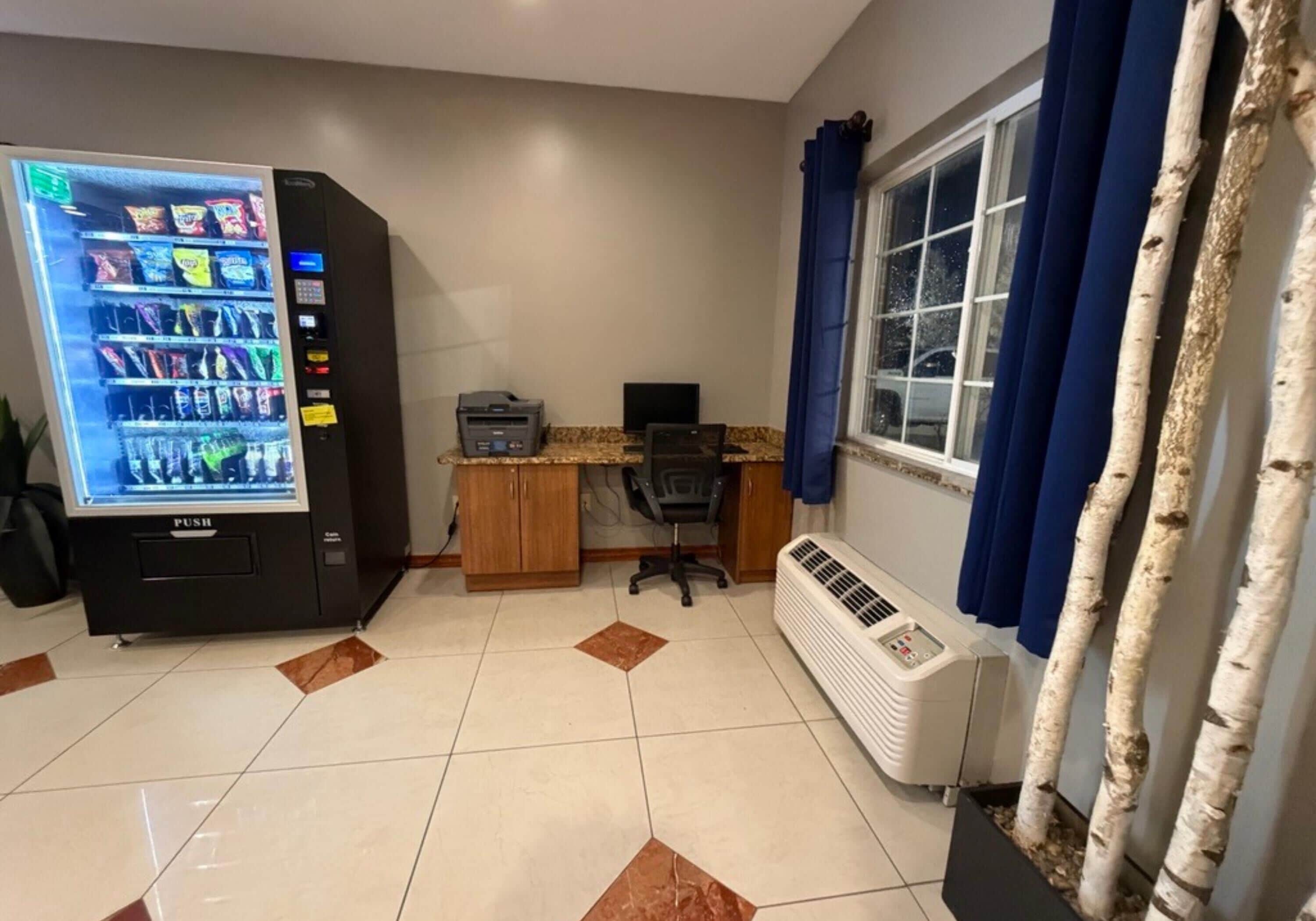 A room with a vending machine, a desk with a computer, a window with curtains, and a radiator.