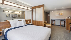 Une chambre d’hôtel avec un grand lit, un bureau avec deux chaises, un miroir et une télévision.