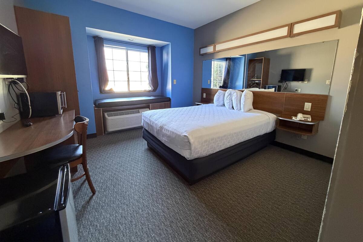 Une chambre d’hôtel équipée d’un lit, d’un bureau, d’une chaise, d’une fenêtre et d’un téléviseur intégré.