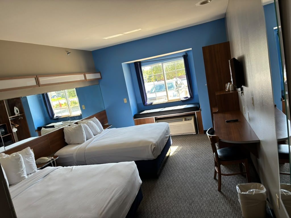 A hotel room with two beds, a desk, a chair, and a TV.