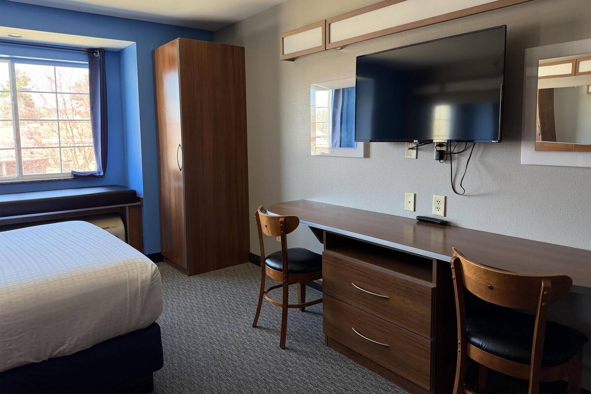 Une chambre à coucher comprenant un lit, un bureau, une chaise, une armoire, un téléviseur et une fenêtre.