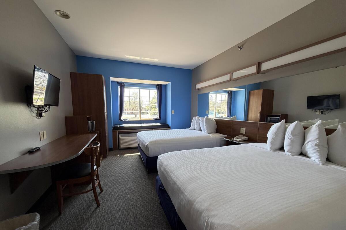 Une chambre d’hôtel avec deux lits, un bureau, une chaise, une télévision et une fenêtre.