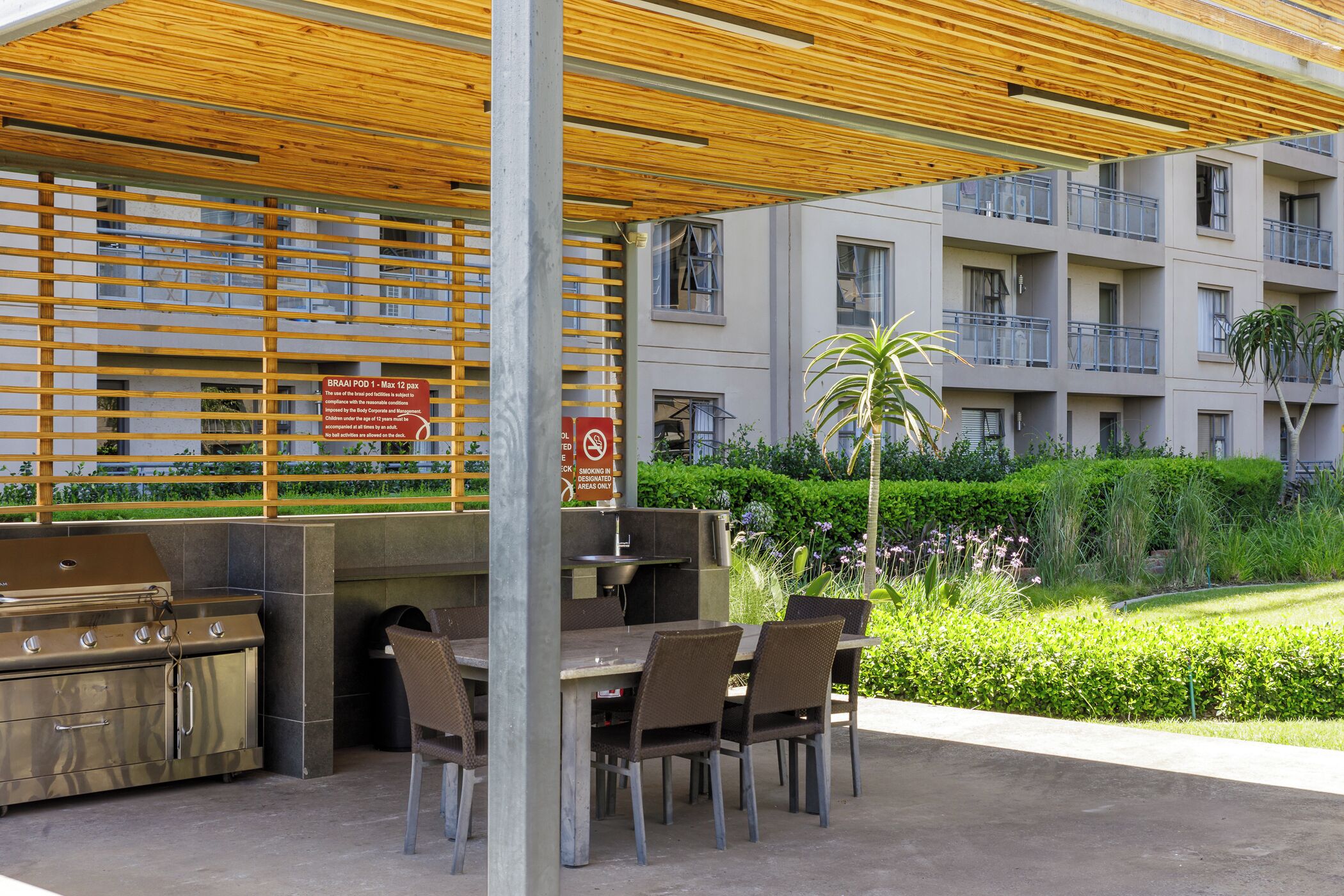 An outdoor patio with a grill and seating area, surrounded by a building with balconies and a sign indicating smoking restrictions.