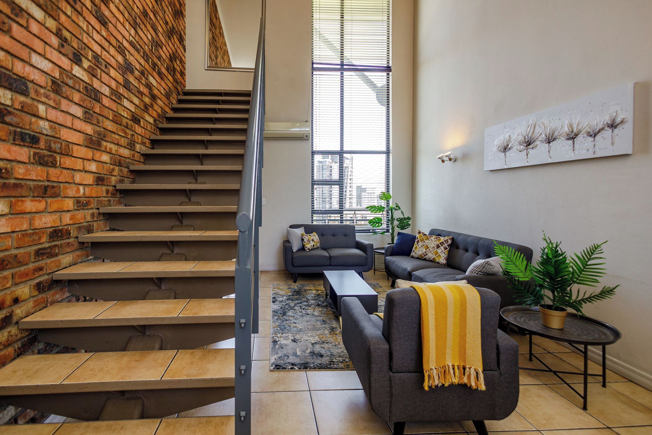Una sala de estar moderna con pared de ladrillo, una escalera y un gran ventanal.