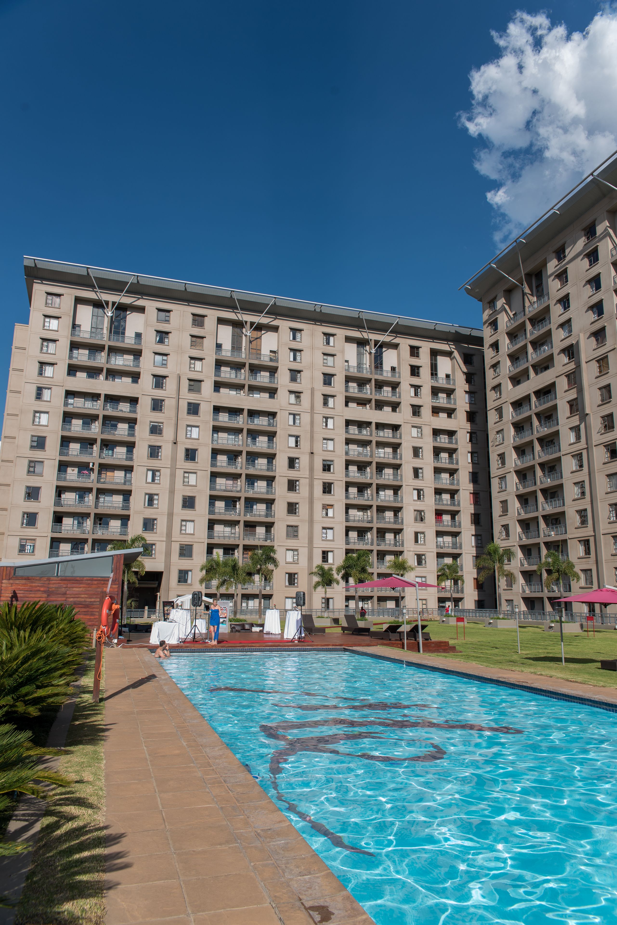 A large hotel with multiple floors, a swimming pool, and palm trees.