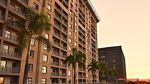 Ein mehrstöckiges Hotel mit Balkonen, einer gepflegten Rasenfläche und einem großen Gebäude im Hintergrund.