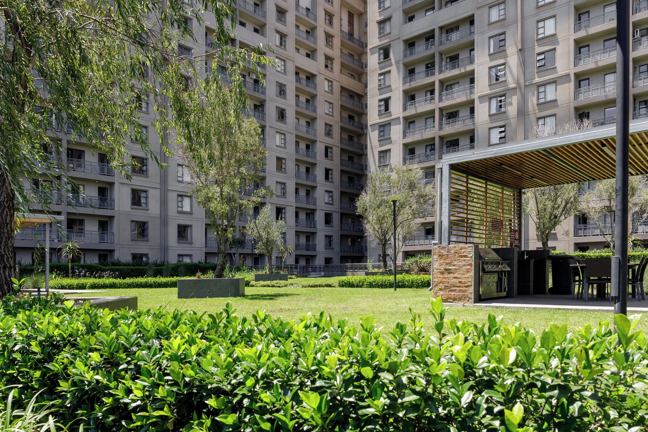 Un edificio residencial de varios pisos con balcones, un patio con césped y una zona de barbacoa.