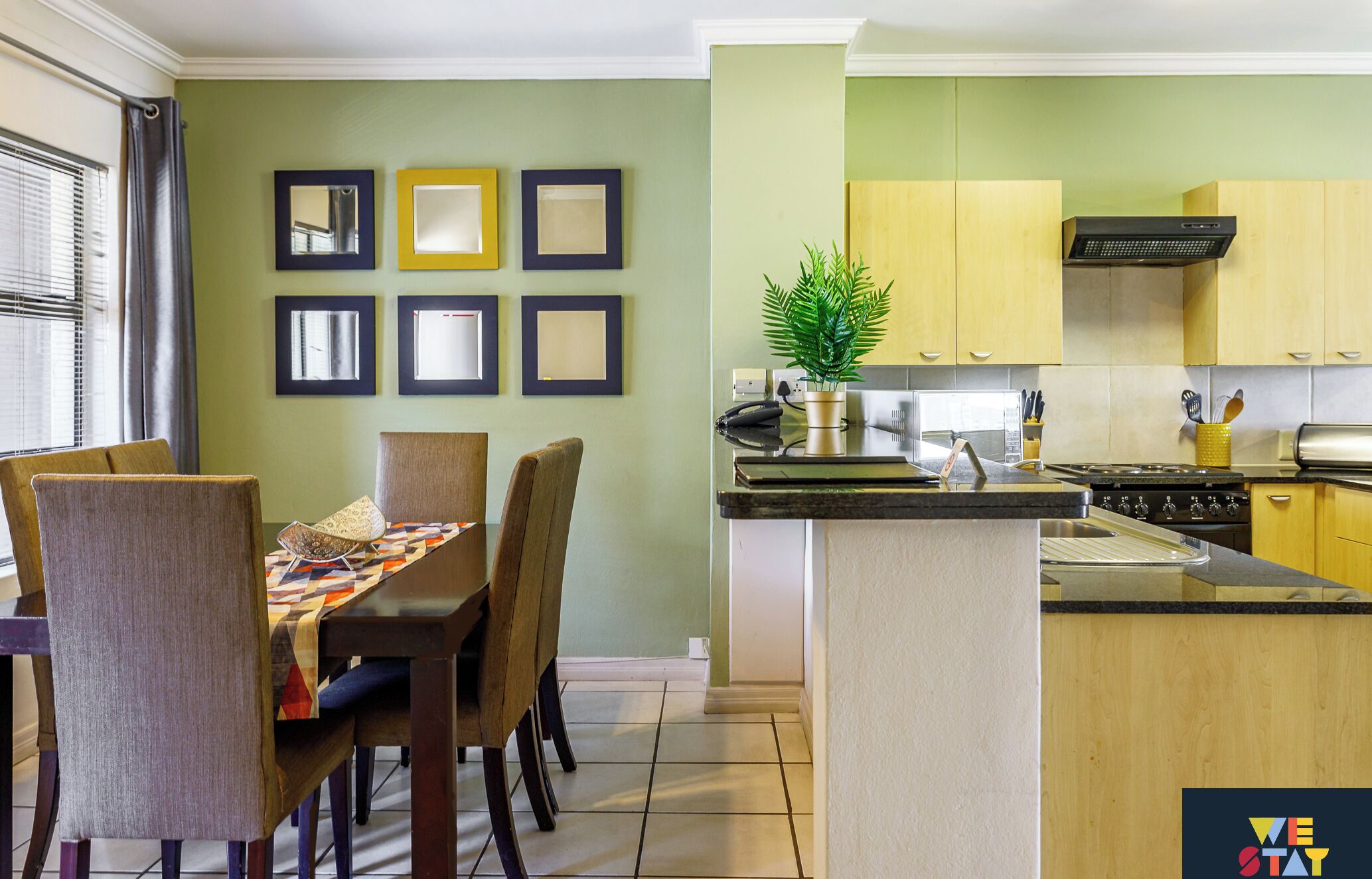 Een moderne keuken met een centraal eiland, houten kastjes en een eethoek met stoelen en een tafel.