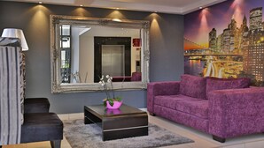 Ein modernes Wohnzimmer mit einem großen Spiegel, einem violetten Sofa, einem schwarzen Couchtisch und einer Stadtansicht als Wandgemälde.