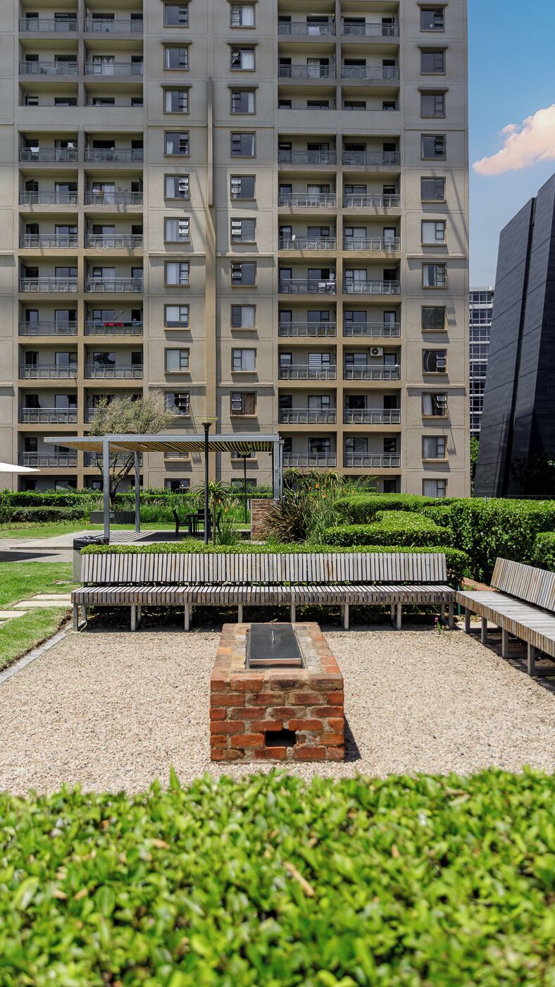 A multi-story residential building with balconies, a paved outdoor area with benches, and a brick fireplace.