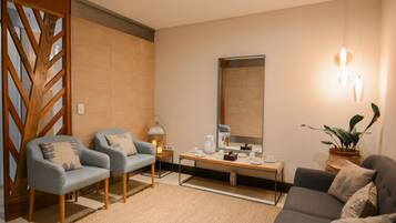 Una sala de estar moderna con dos sillones, un sofá, una mesita de centro, una mesita auxiliar, una lámpara de pie, un espejo y una planta en maceta.