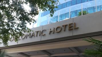 El exterior del Hotel Diplomatic, con una fachada moderna, amplias ventanas de vidrio y una entrada destacada con escalones que conducen a la puerta.
