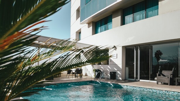 A swimming pool with a modern building in the background. - Diplomatic Hotel (Mendoza)