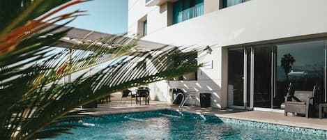 Una piscina al aire libre, sombrillas, sillones reclinables de piscina