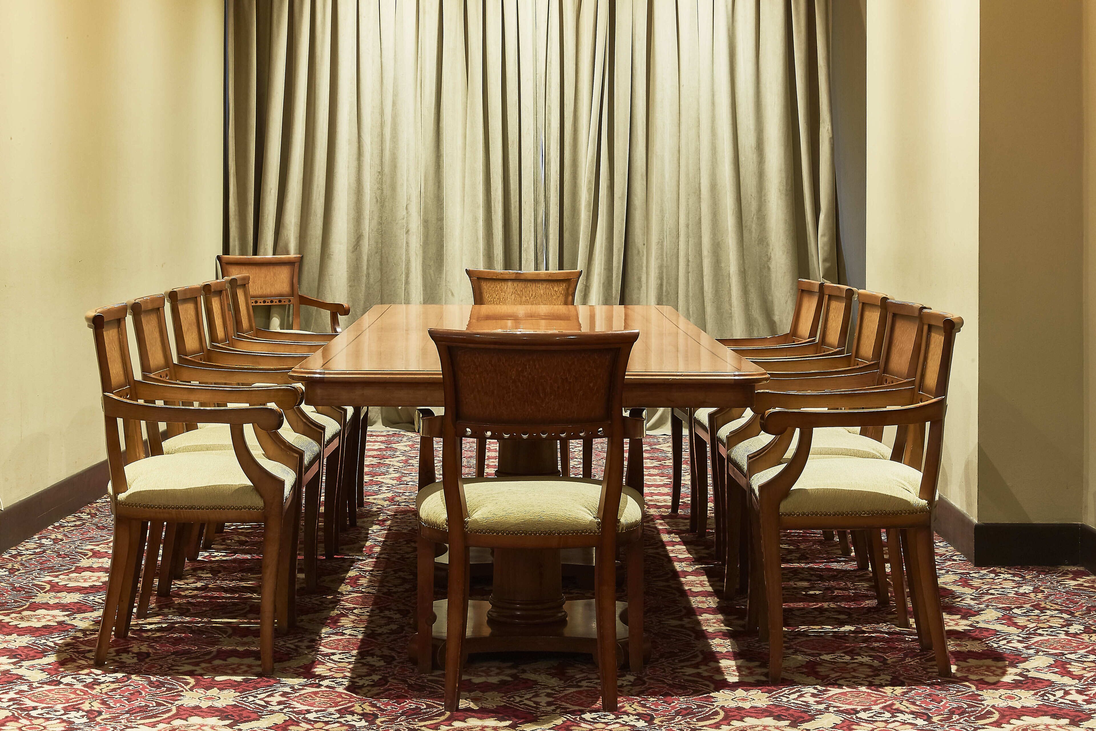 Un salón de conferencias con una gran mesa rectangular rodeada de sillas de madera con asientos acolchados.