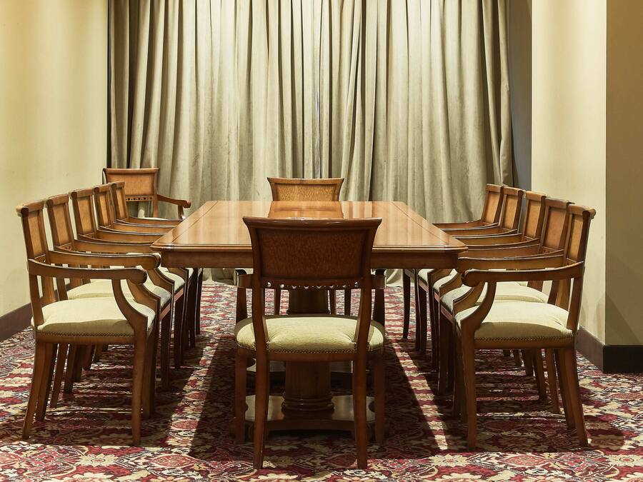 Un salón de conferencias con una gran mesa rectangular rodeada de sillas de madera con asientos acolchados.