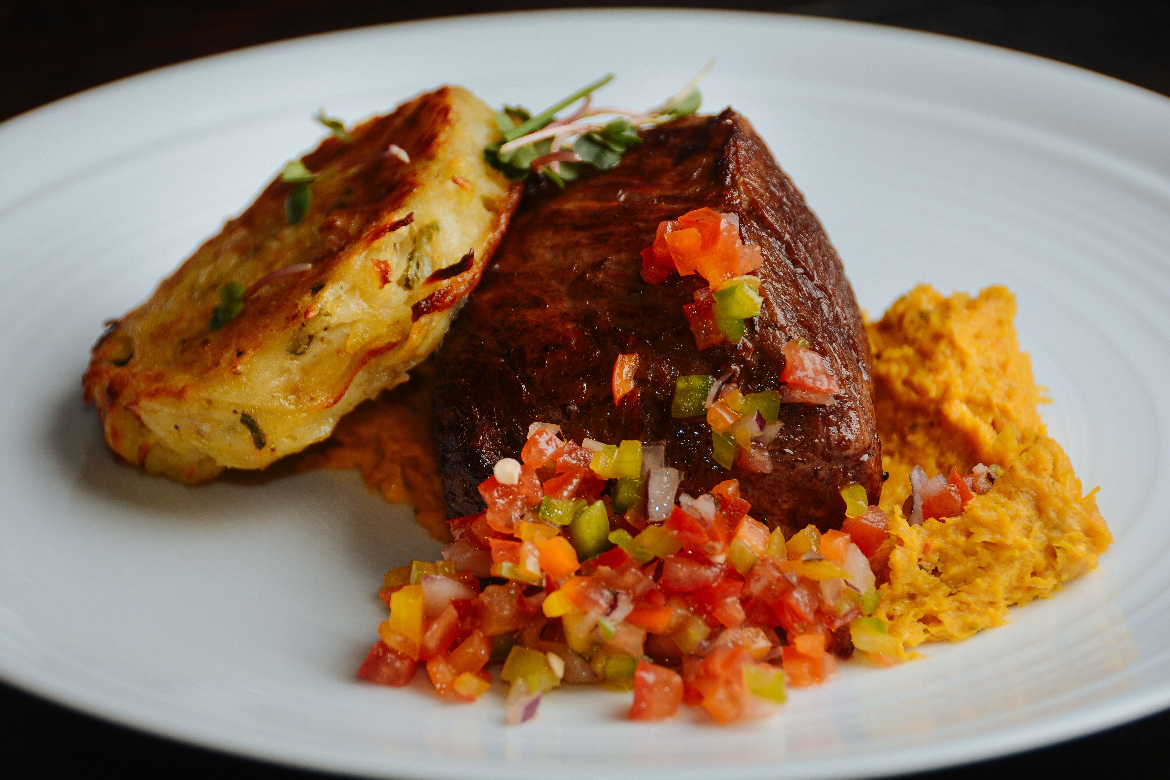 A plate with a piece of meat, a side of potatoes, and a salsa.