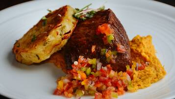 A plate with a piece of meat, a side of potatoes, and a salsa.
