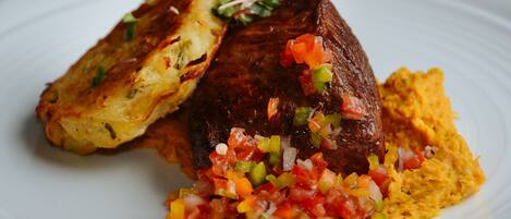 A plate with a piece of meat, a side of potatoes, and a salsa.