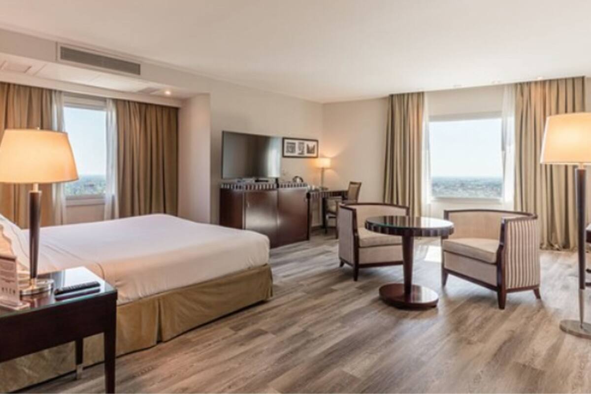 A hotel room with a bed, a desk, a chair, a table, and a TV.