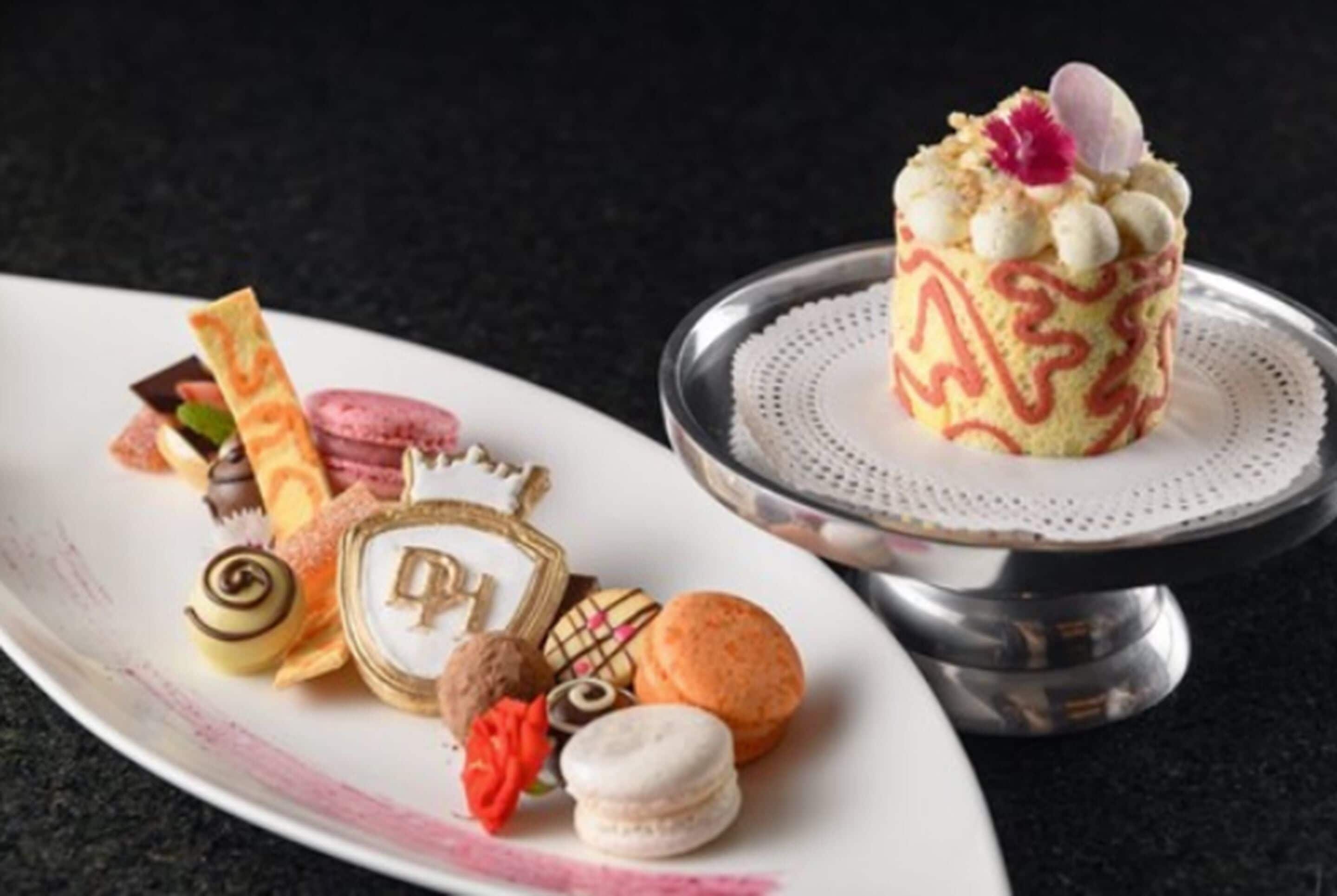 Una selezione di dolci su un piatto bianco e una torta su un piedistallo d'argento.
