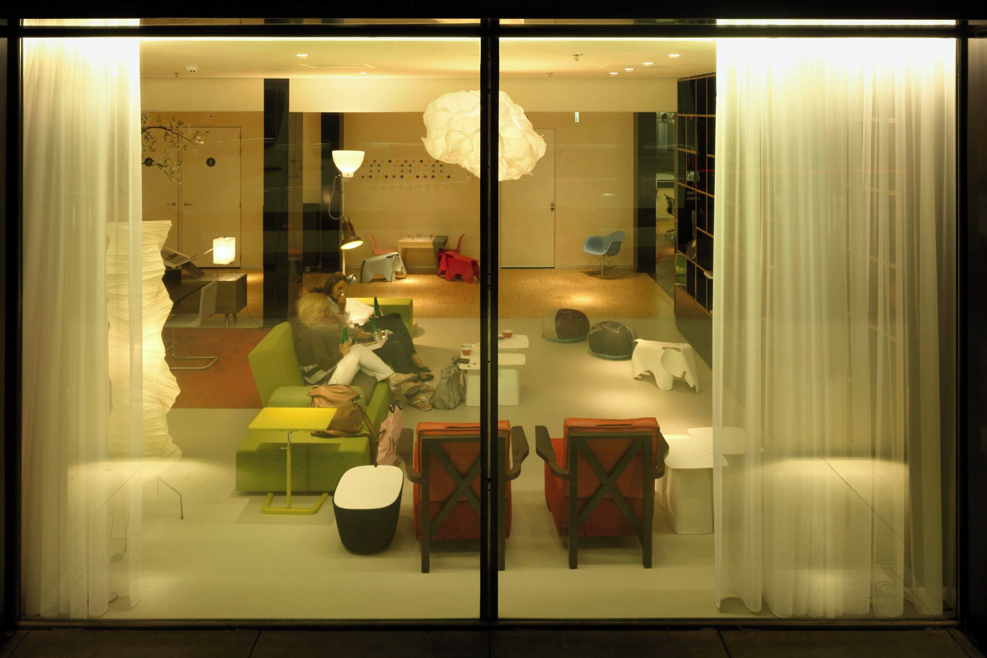 A modern interior with a glass partition, a green sofa, a small table, and a red chair.
