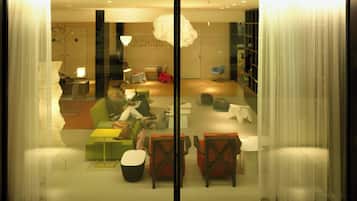 A modern interior with a glass partition, a green sofa, a small table, and a red chair.