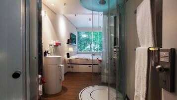 Un baño moderno con cabina de ducha de vidrio, inodoro, lavamanos y cama con vista a la ventana.