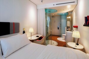 Una habitación de hotel moderna con una cama, un escritorio, una silla, un baño con espejo y un inodoro.
