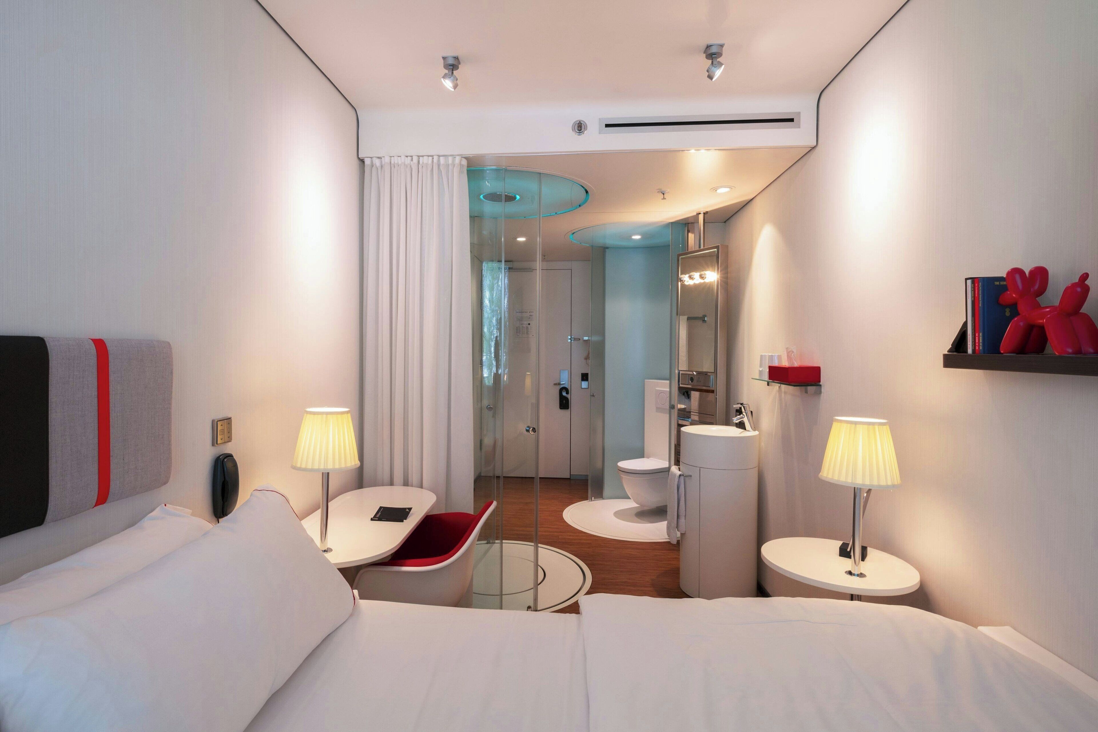 Una habitación de hotel moderna con cama, mesitas de noche, escritorio, zona de ducha y baño.
