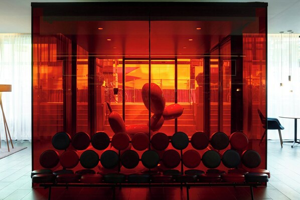 A modern interior with a seating area featuring circular and oval chairs, a glass partition, and a visible staircase. - citizenM Amsterdam South (Amsterdam)
