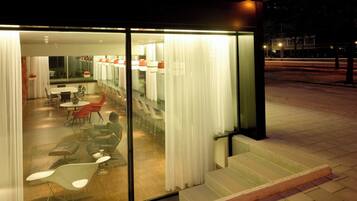 A modern hotel interior with a dining area, a kitchen, and a bar.
