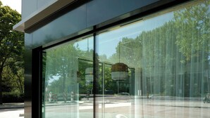 A modern building with large glass windows reflecting a street scene.