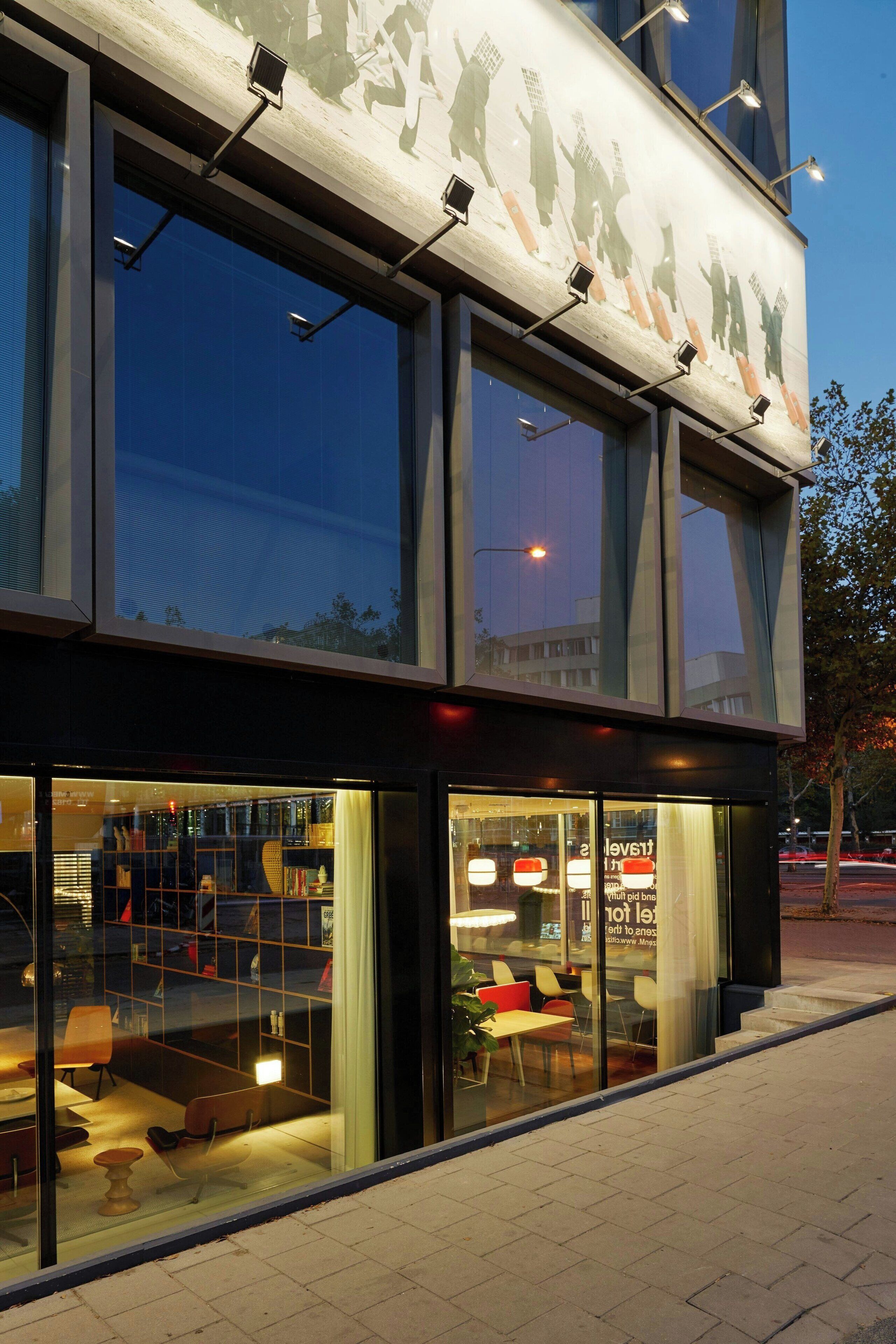 A modern building with large windows and a glass facade, featuring a seating area inside.