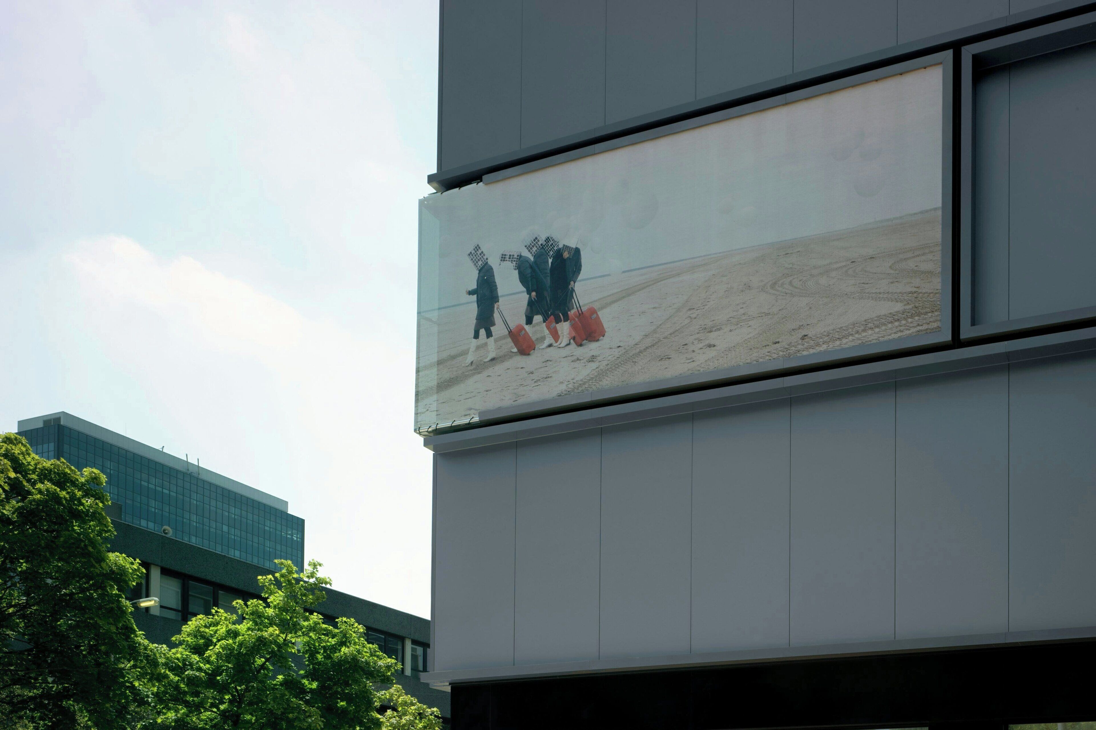 A modern building with a large billboard displaying a scene of people walking with luggage.