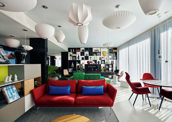 Una sala moderna con un sofá rojo, sillones verdes y un comedor con sillas rojas.