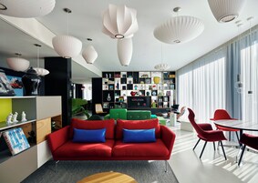 Una sala moderna con un sofá rojo, sillones verdes y un comedor con sillas rojas.